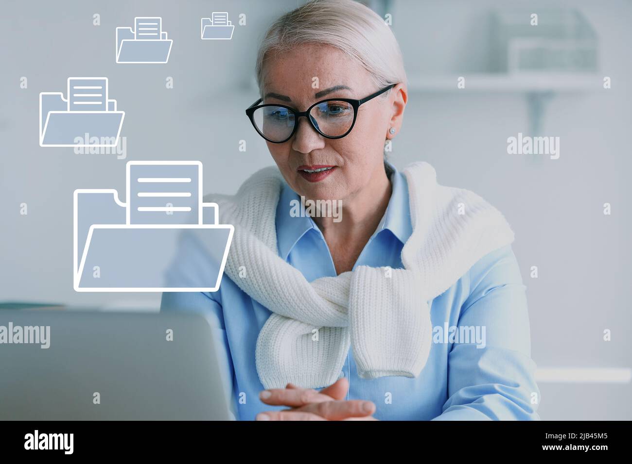 Donna d'affari matura con laptop e file digitali su schermo virtuale in ufficio Foto Stock