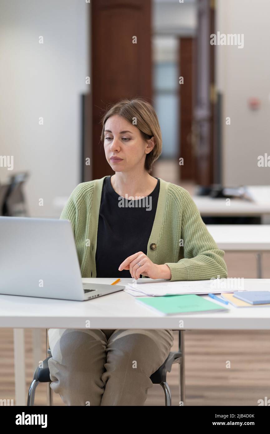 Studentessa di mezza età focalizzata sul lavoro su laptop nello spazio di coworking, ottenendo il secondo grado Foto Stock