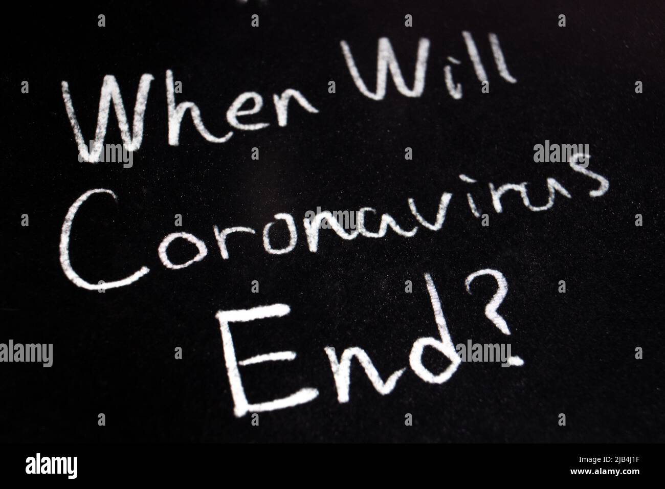 Primo piano della frase quando Coronavirus finirà? scrivendo a mano con gesso bianco su lavagna. La superficie della lavagna è polverosa e ruvida Foto Stock