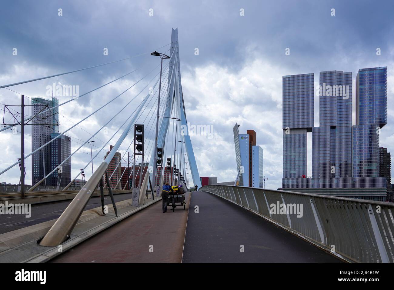 Un uomo spinge la sua moto da carico in tempo ventoso attraverso il ponte Erasmus a Rotterdam, Paesi Bassi, 5/27/22 Foto Stock