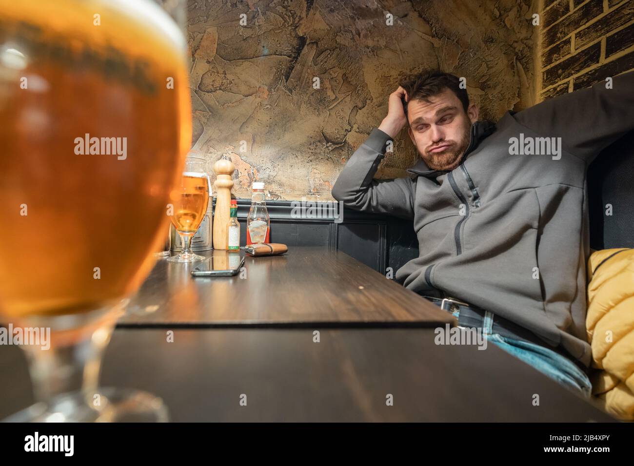 Persona completamente ubriaca in un bar che guarda verso un grande bicchiere di birra. Alcol si male per te uomo, ovviamente. Foto Stock