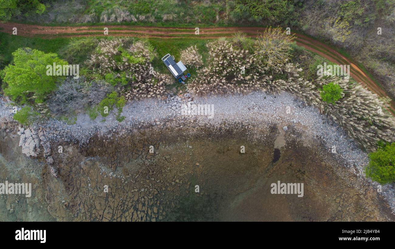 Vista verticale di un furgone o camper parcheggiato proprio accanto al mare o alla spiaggia. Sterrato pista sopra e fresco mare calmo sotto. Foto Stock
