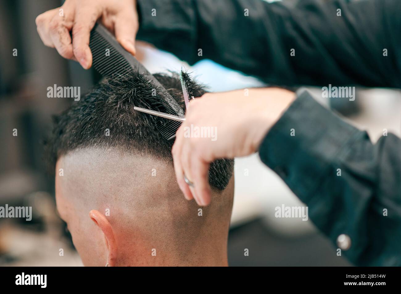 Crop unrecognized barber taglio capelli neri anonimi del cliente maschile con forbici affilate in moderno parrucchiere su sfondo sfocato Foto Stock