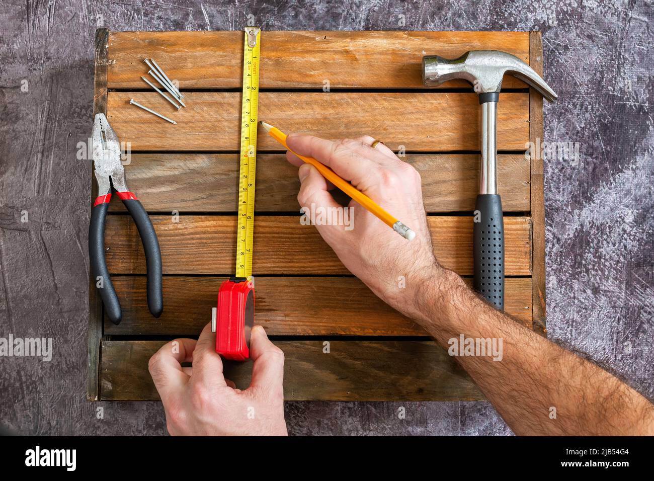 Misure usando le misure della roulette per la riparazione. Mani con l'attrezzo. Set di attrezzi per la riparazione domestica. Martello, pinze, chiodi, dadi. Foto Stock