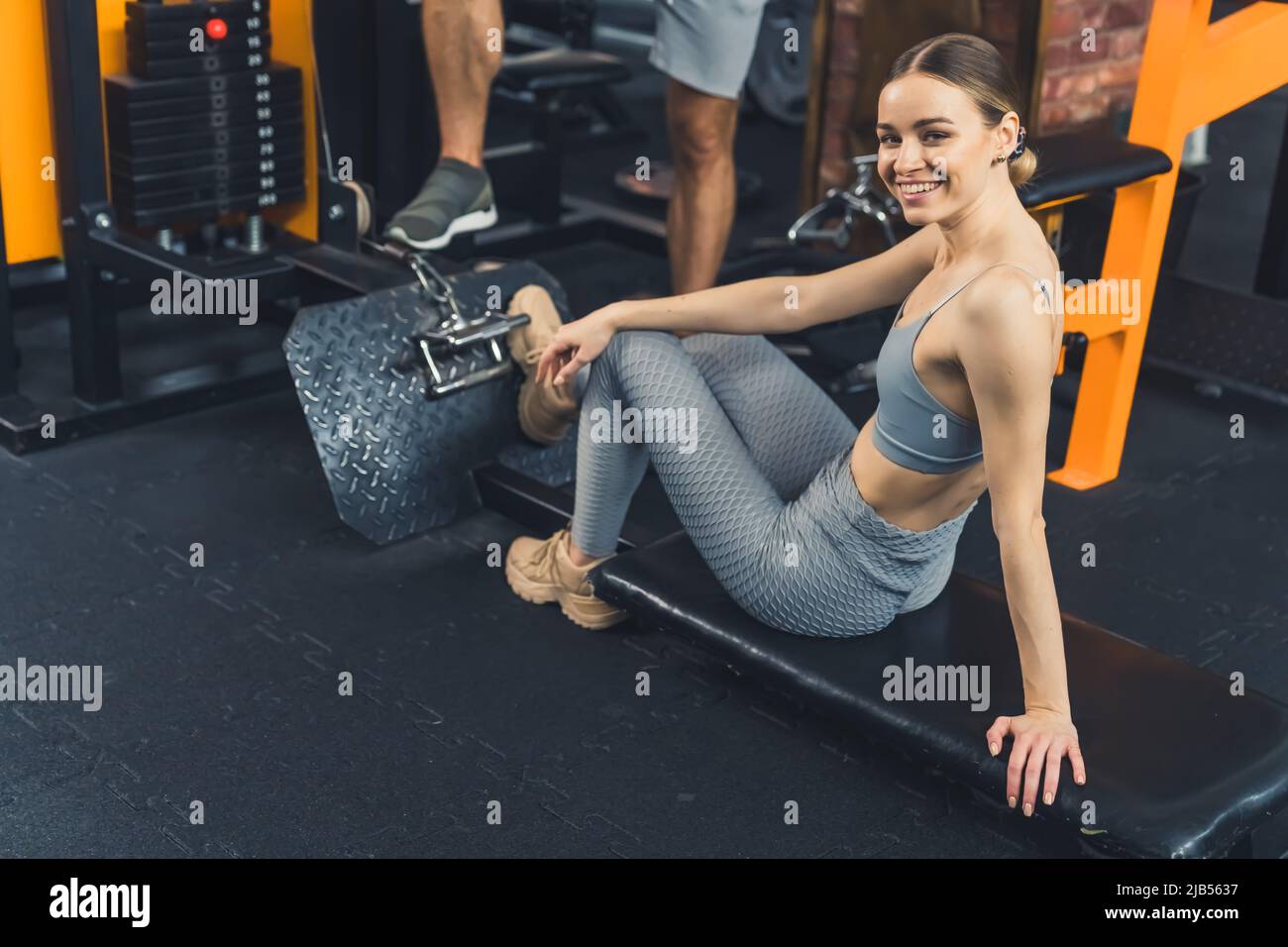 Allegro eccitata giovane donna europea seduta su una panca nera in palestra, avendo una pausa tra le esercitazioni su una macchina vogatrice. Foto di alta qualità Foto Stock