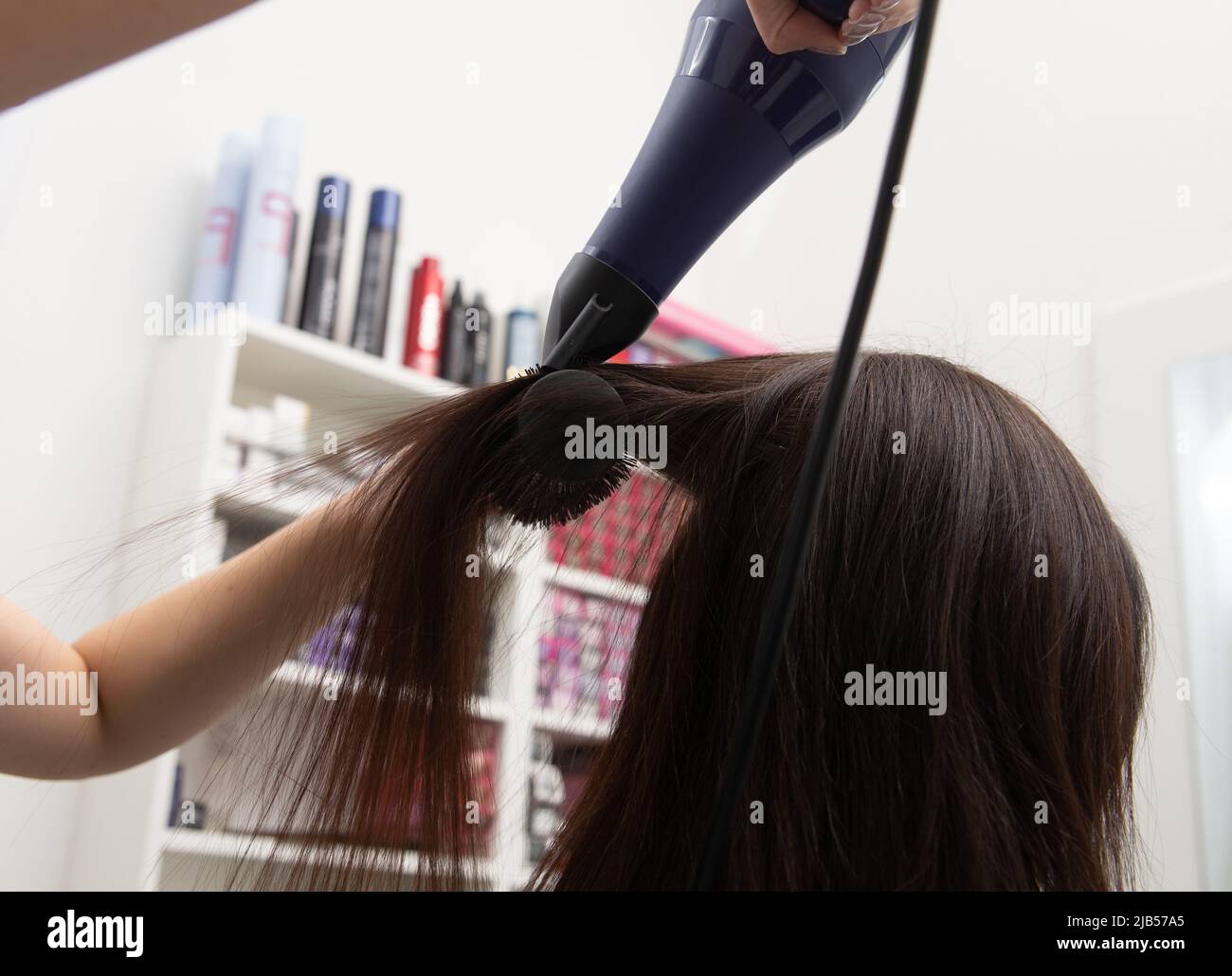 Donna al parrucchiere soffiare asciugando i capelli. Sullo sfondo ci sono ripiani con una grande selezione di tinture per capelli Foto Stock