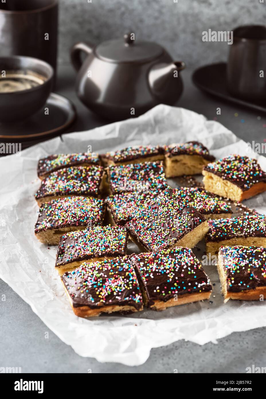 Deliziosa torta fatta in casa con glassa al cioccolato fondente e zucchero colorato cospargere su carta da forno. Stile rustico. Messa a fuoco selettiva. Foto Stock