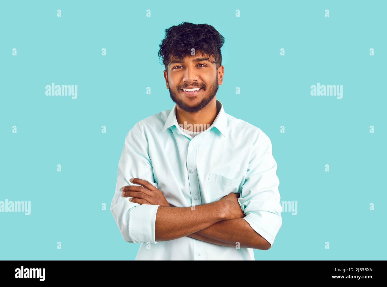 Ritratto di felice uomo indiano o arabo in camicia in piedi con le braccia piegate e sorridenti Foto Stock