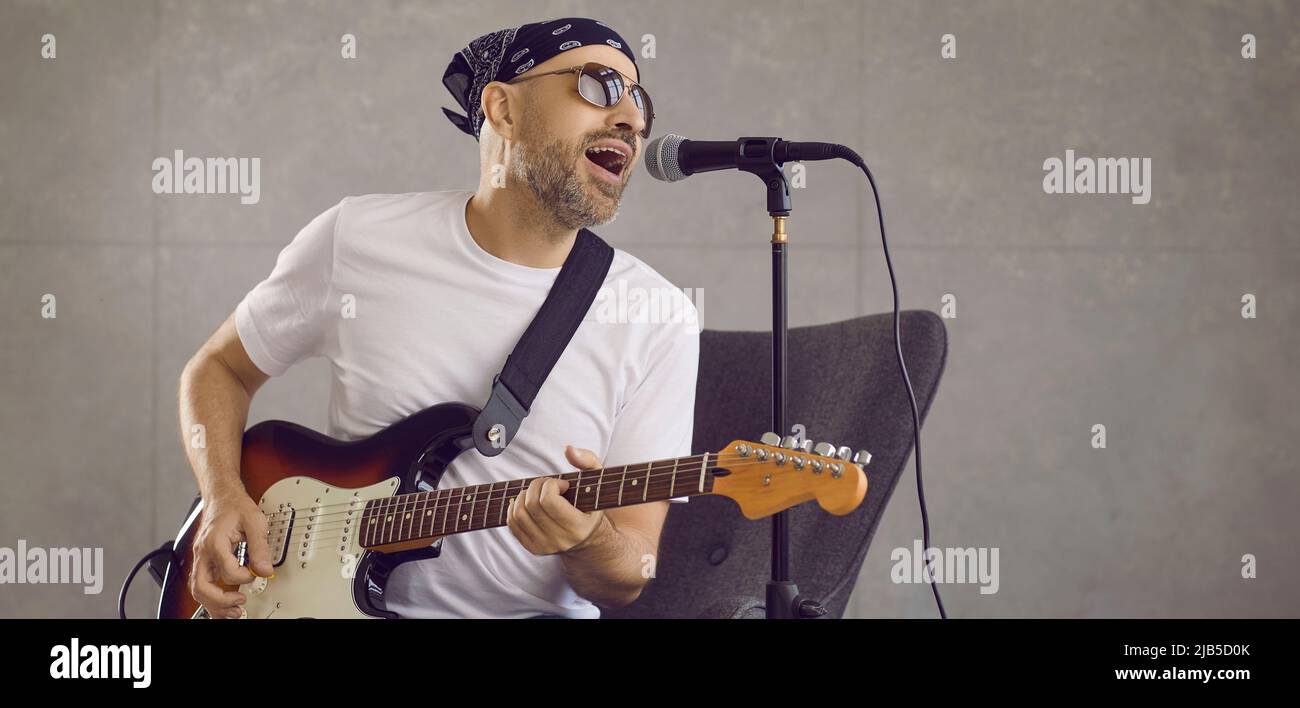 Musicista rock in bandana e occhiali da sole che suonano chitarra elettrica e cantano in studio Foto Stock