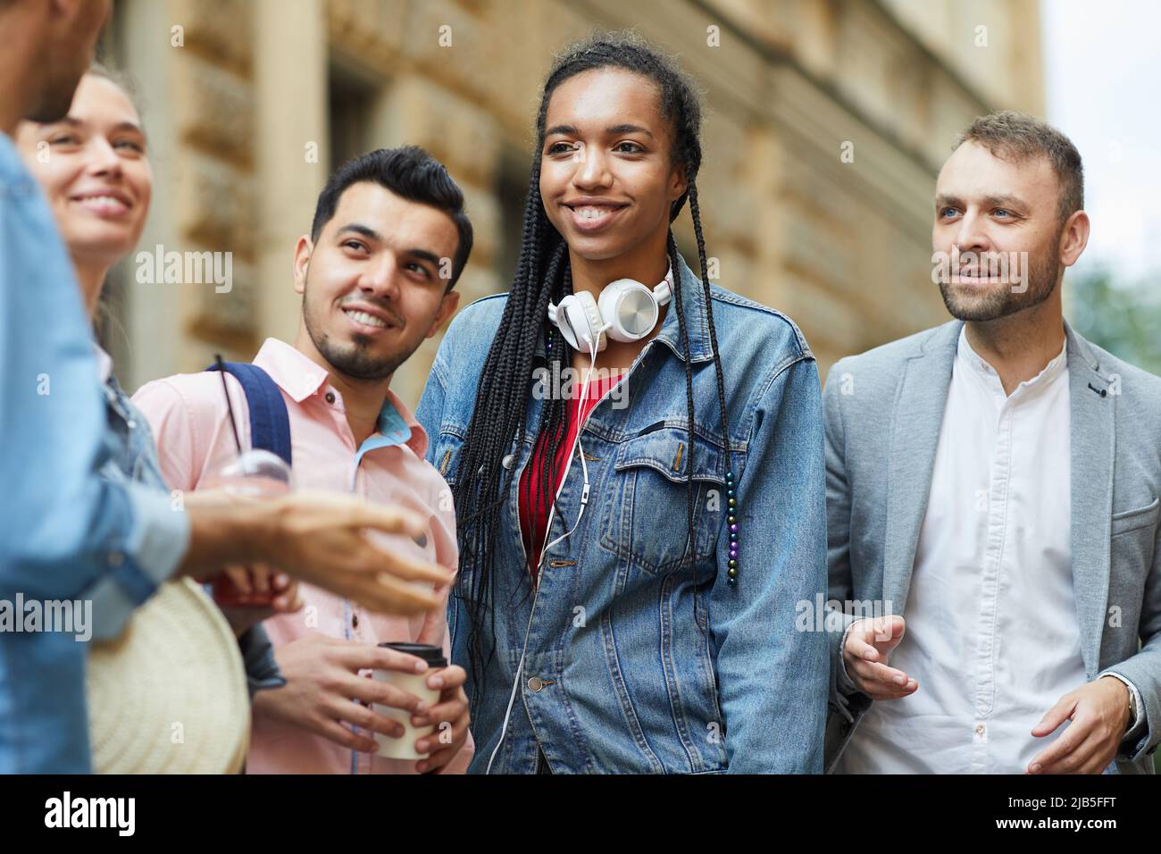 Gruppo di giovani amici multietnici positivi in abiti casual in piedi sulla strada della città e chiacchierare insieme Foto Stock