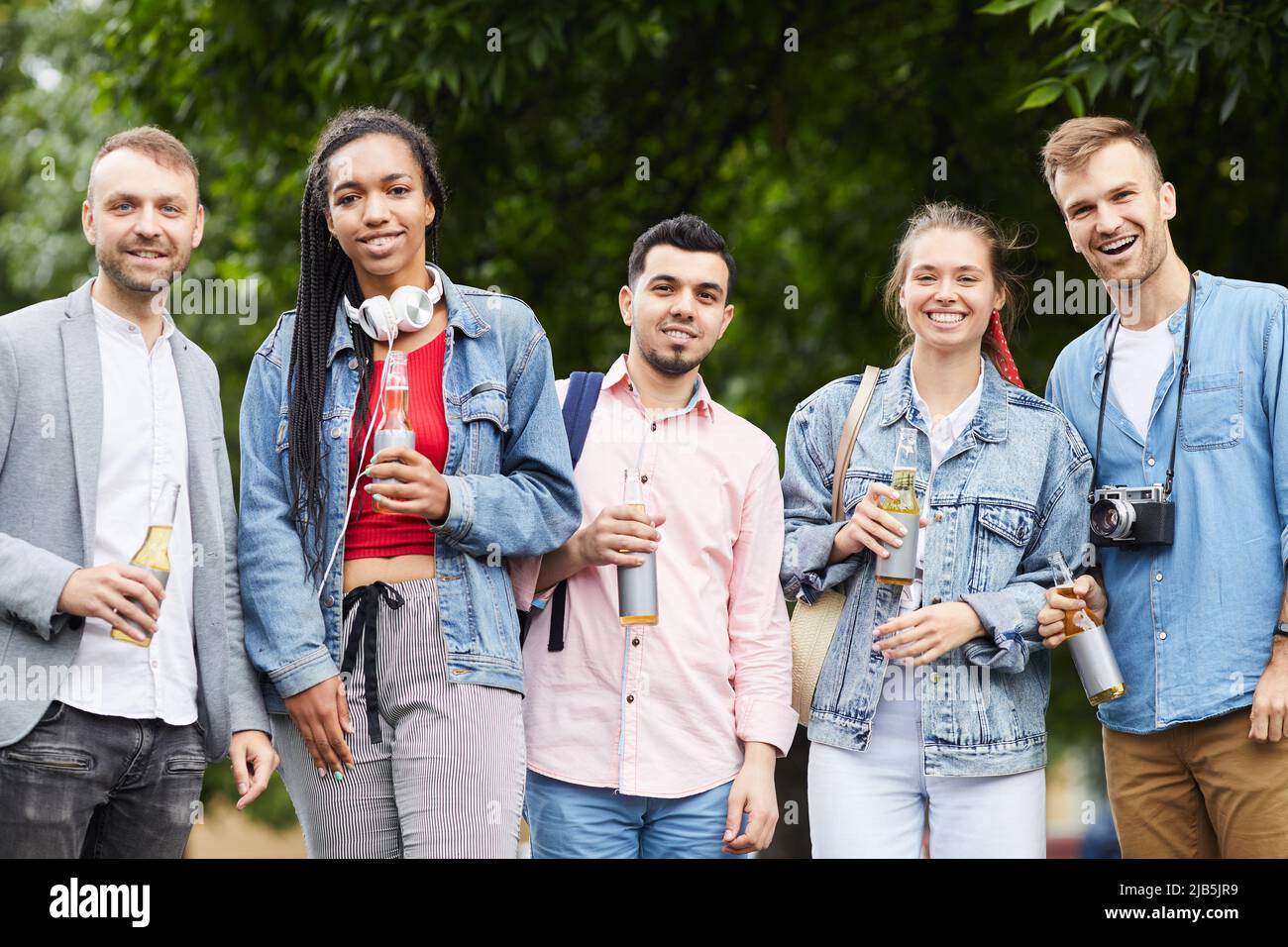 Gruppo di giovani amici multietnici positivi in abiti casual in fila e bere birra analcolica all'aperto Foto Stock