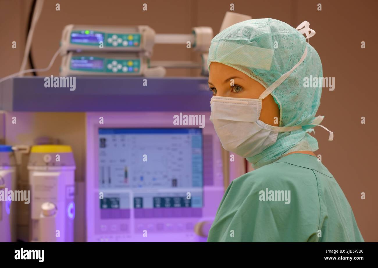 In una sala operatoria è presente un infermiere anestetico. Si vede vestita di abbigliamento medico sterile verde con una maschera sul viso. Foto Stock