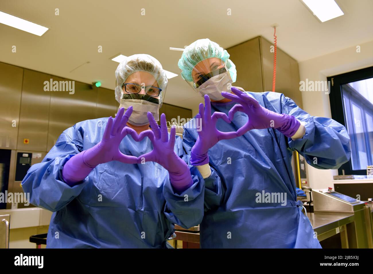 Due donne sono considerate lavoratori di igiene medica. Essi formano le loro dita a forma di cuore per mostrare che sono felici con il loro ritmo di lavoro. Foto Stock