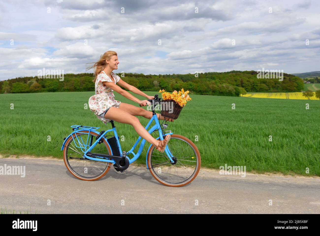 Una giovane donna spensierata ama la sua nuova bicicletta elettrica ibrida. Si prende per un giro rilassante nel paese senza usare i pedali della bicicletta. Foto Stock