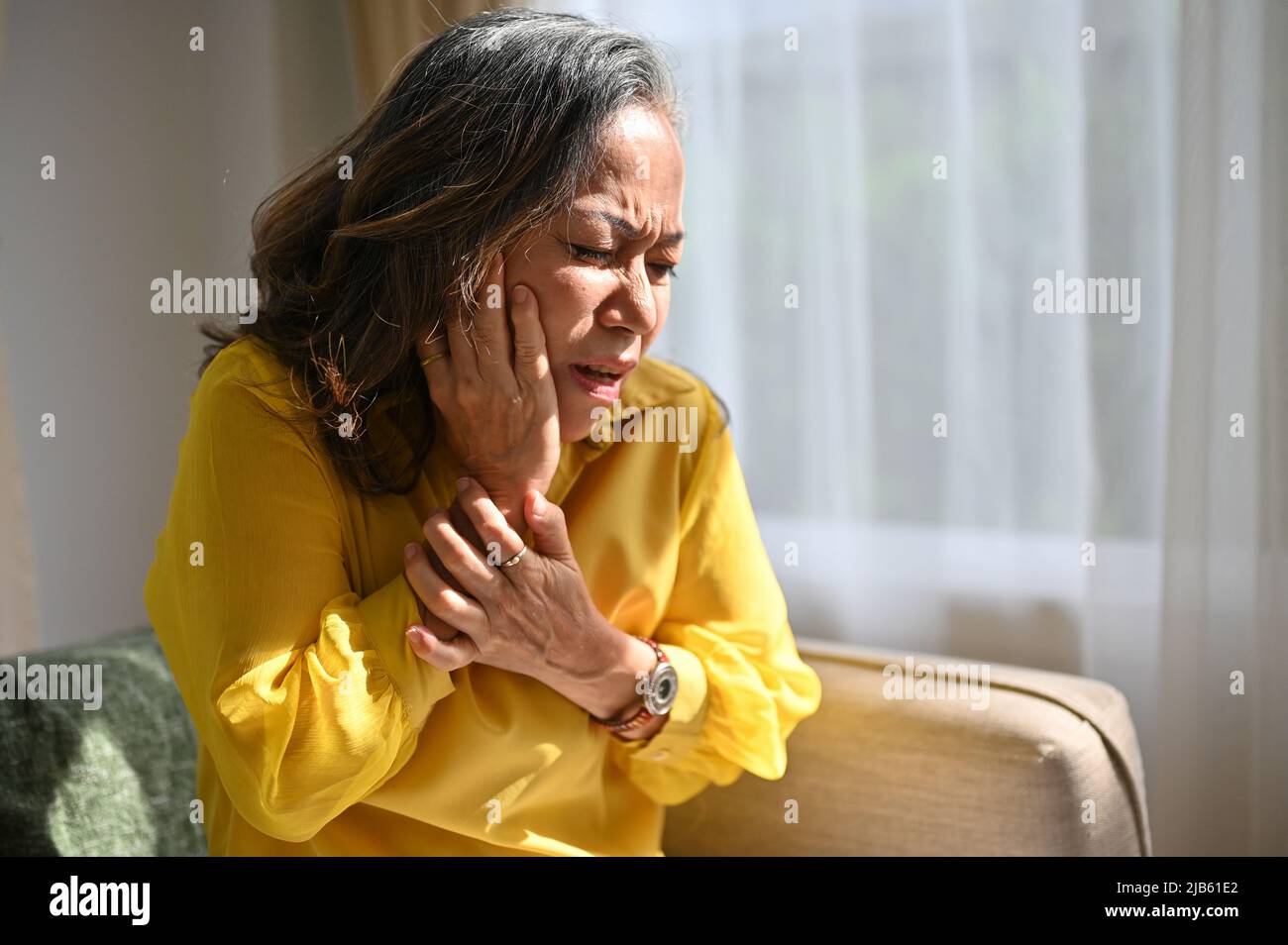 La donna asiatica invecchiata tocca la guancia che soffre di improvviso dolore ai denti. Vecchia signora con un'espressione dolorosa del dente. Concetto di malattia dentale Foto Stock