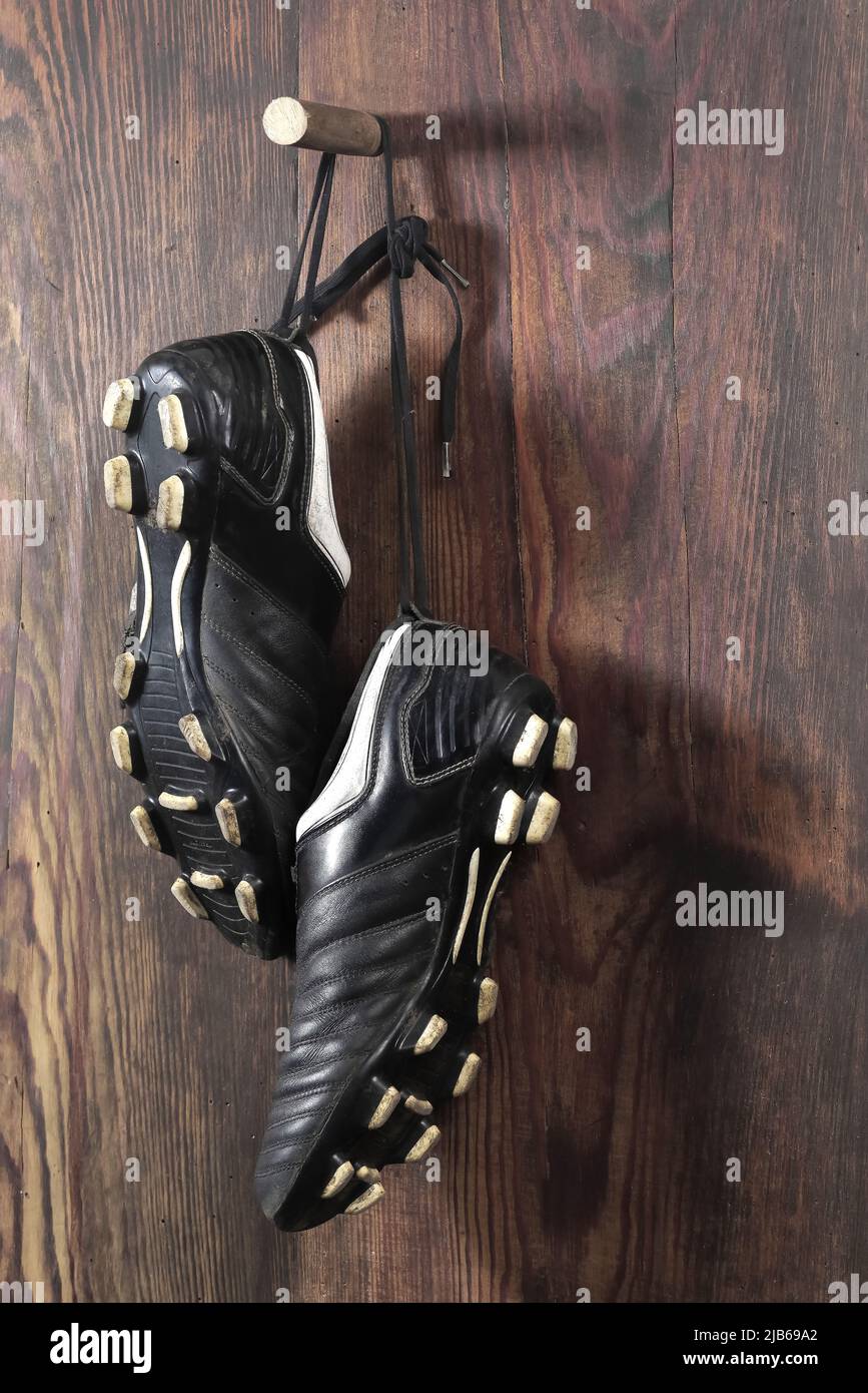 Un paio di stivali da calcio appesi su un muro di legno. La fine della carriera calcistica Foto Stock