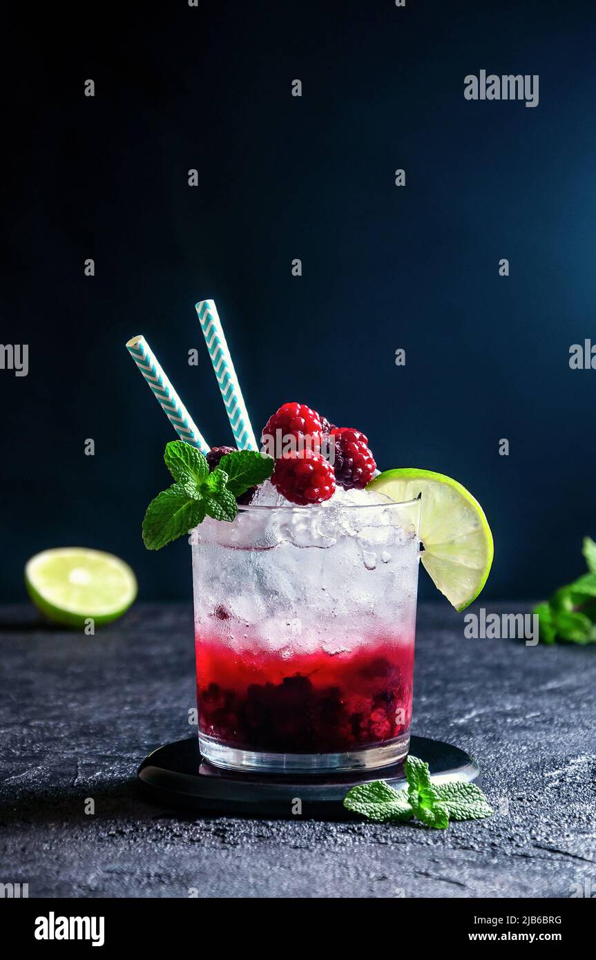 Cocktail alcolico con rum o Vodka, soda, lampone e purea di BlackBerry, lime e menta in vetro su sfondo grigio scuro Foto Stock