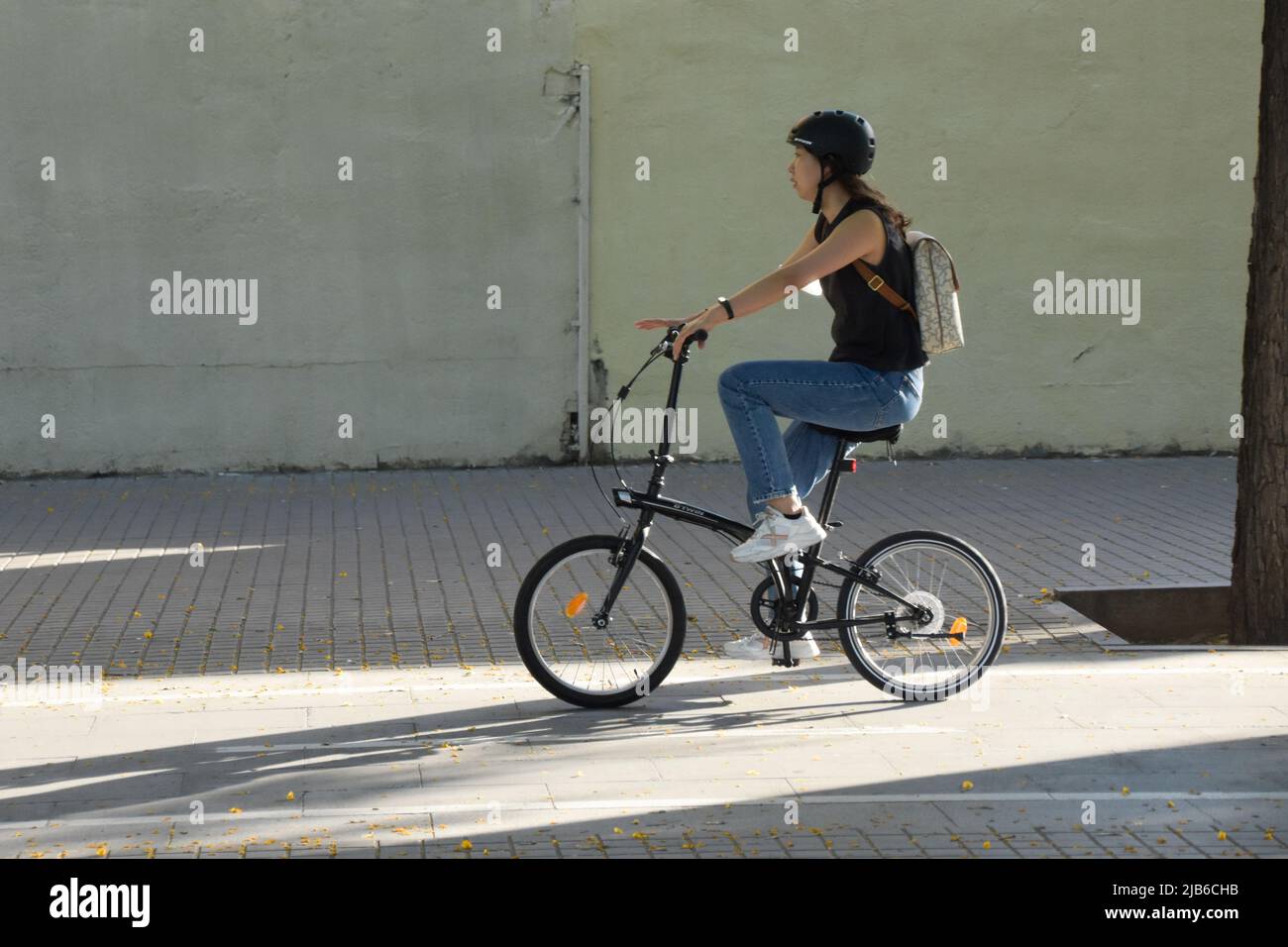 Una giovane donna con casco e zaino sta guidando una bicicletta in una strada. Foto Stock