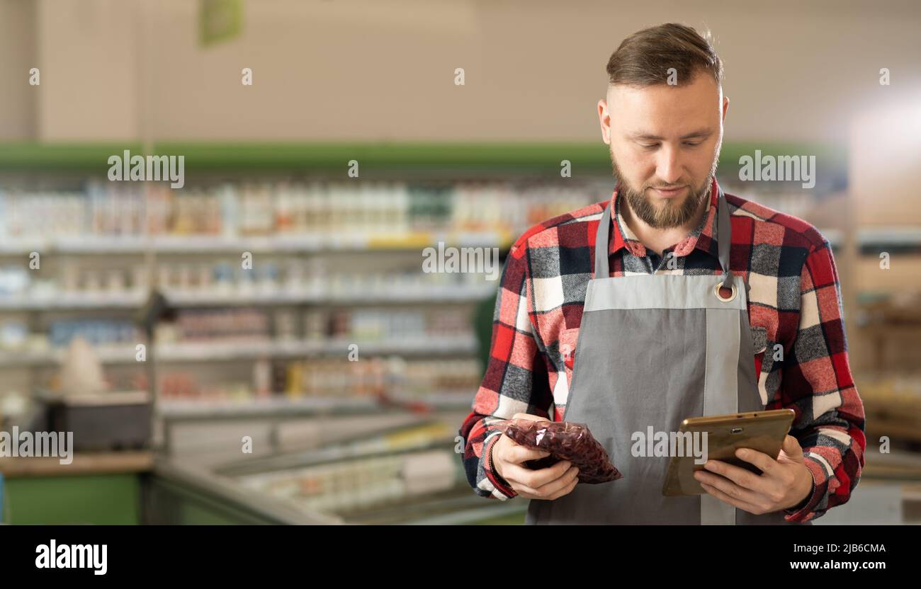 Un impiegato sicuro del supermercato che lavora con un tablet digitale cerca il prezzo del prodotto online, la tecnologia e il lavoro Foto Stock