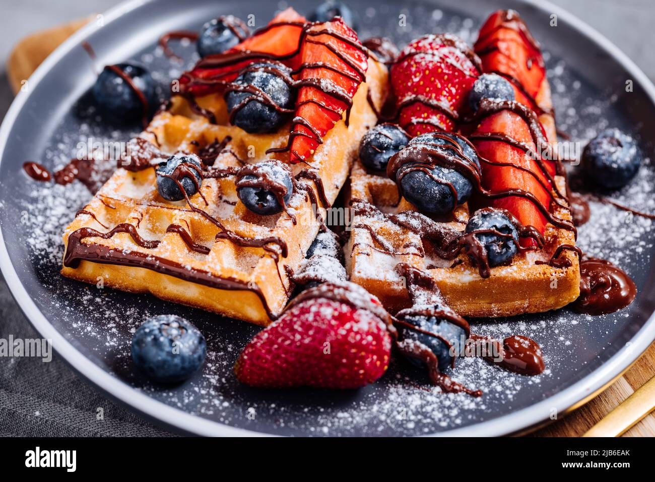 Waffle belgi con cioccolato, fragola, mirtilli e zucchero in polvere su piatto scuro Foto Stock