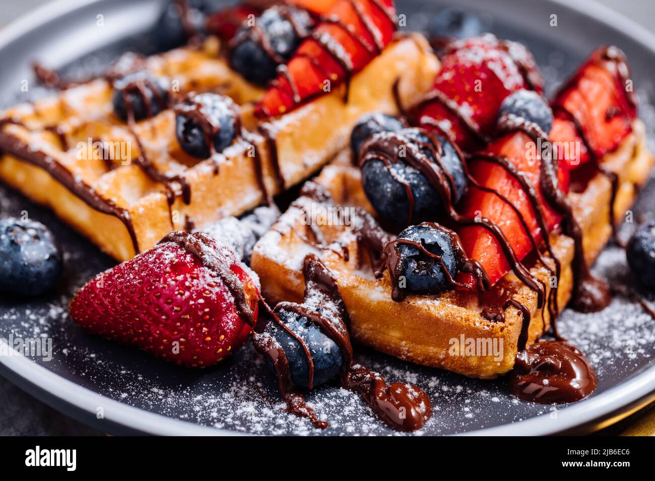 Waffle belgi con cioccolato, fragola, mirtilli e zucchero in polvere su piatto scuro Foto Stock