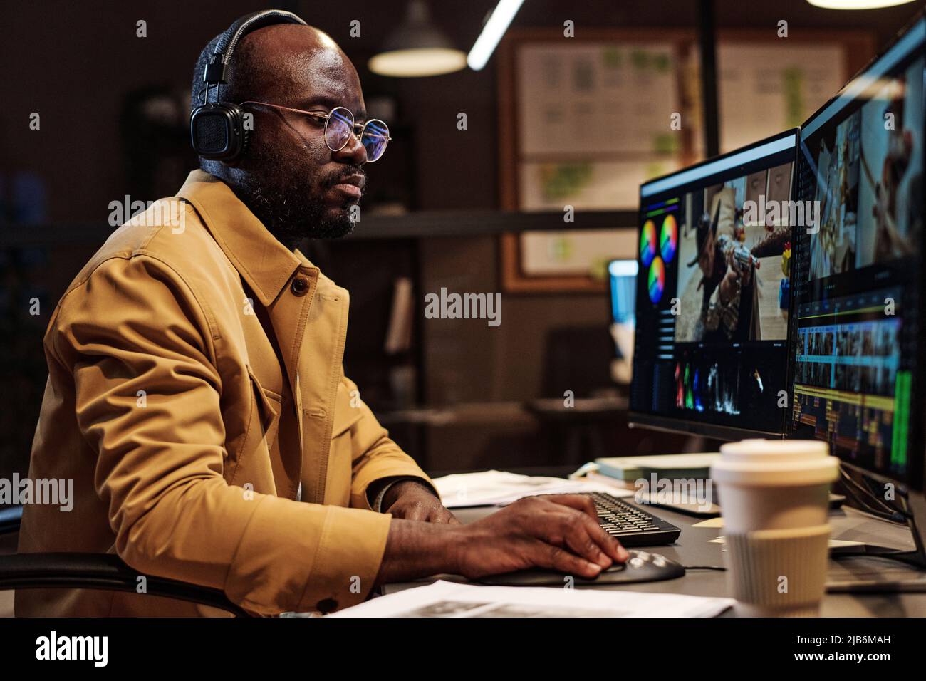 Serio colorista africano in occhiali concentrandosi sul suo lavoro a tavola, lui fare foto editing sul computer Foto Stock