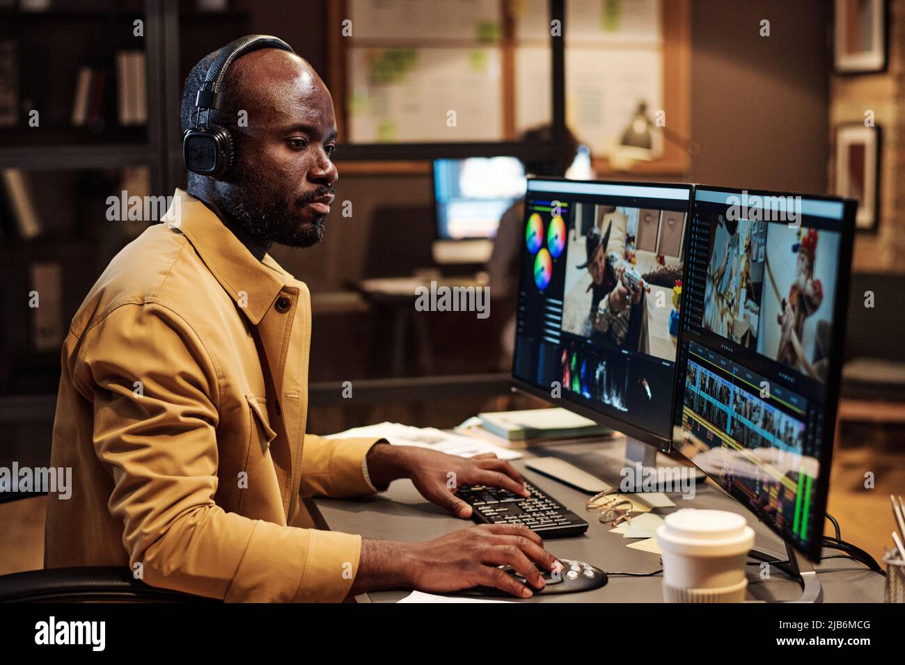 Colorista africano concentrandosi sul suo lavoro in ufficio fino a tarda sera, egli editing di filmati su computer Foto Stock