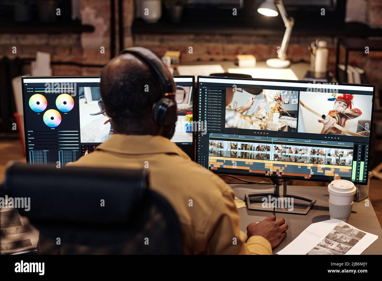 Vista posteriore dell'editor o del video designer in cuffie che si trovano davanti allo schermo del computer e lavorano con nuovi contenuti Foto Stock