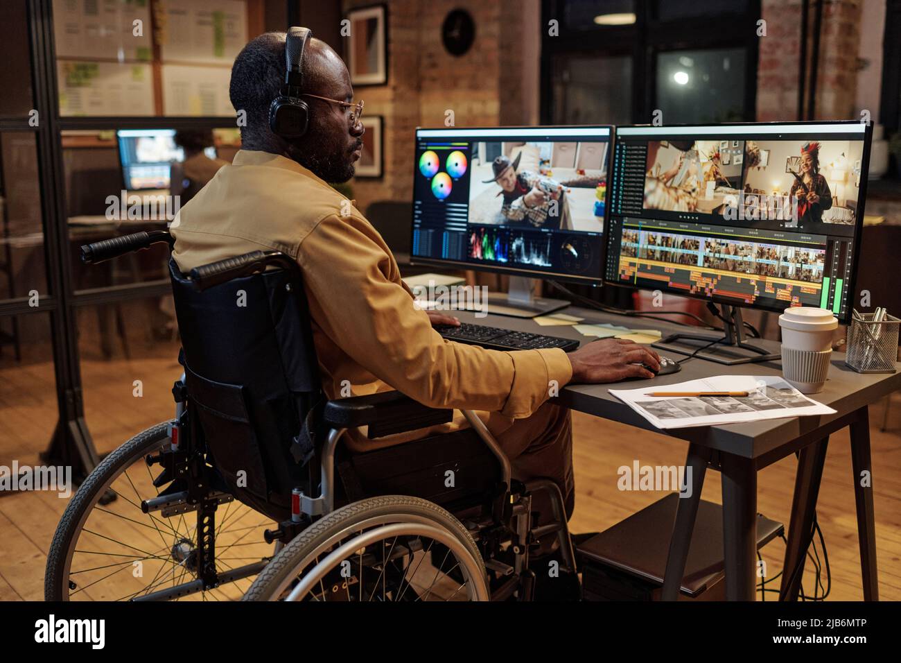 Vista posteriore dell'editor in cuffie in sedia a rotelle davanti allo schermo del computer e al lavoro con nuovi contenuti Foto Stock