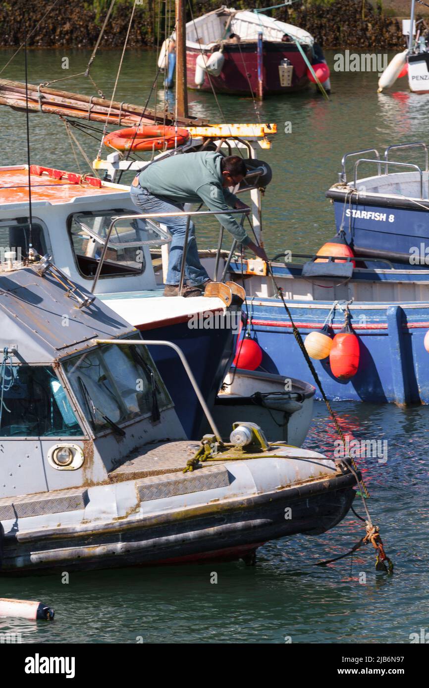 Un pescatore alla prua della sua barca da pesca tira le linee di ormeggio a bordo: Vita nel villaggio portuale di Porthleven, Cornovaglia Foto Stock