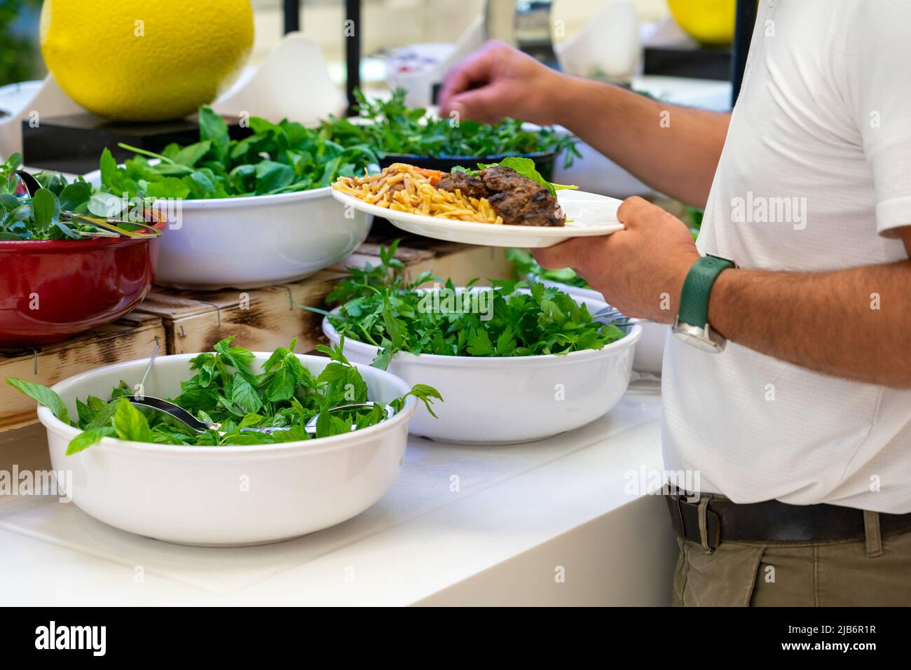 Un uomo sceglie un'insalata dal bar con insalata di erbe fresche al buffet dell'hotel. Cibo salutare Foto Stock
