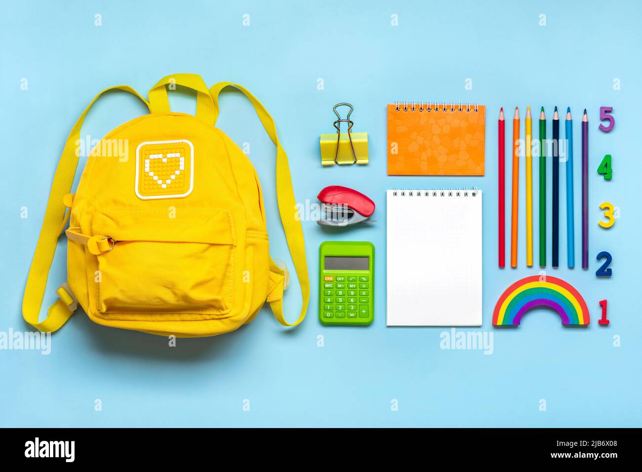 Torna alla scuola, concetto di istruzione zaino giallo con forniture scolastiche - notebook, penne, raser rainbow, numeri isolati su sfondo blu Vista dall'alto Foto Stock