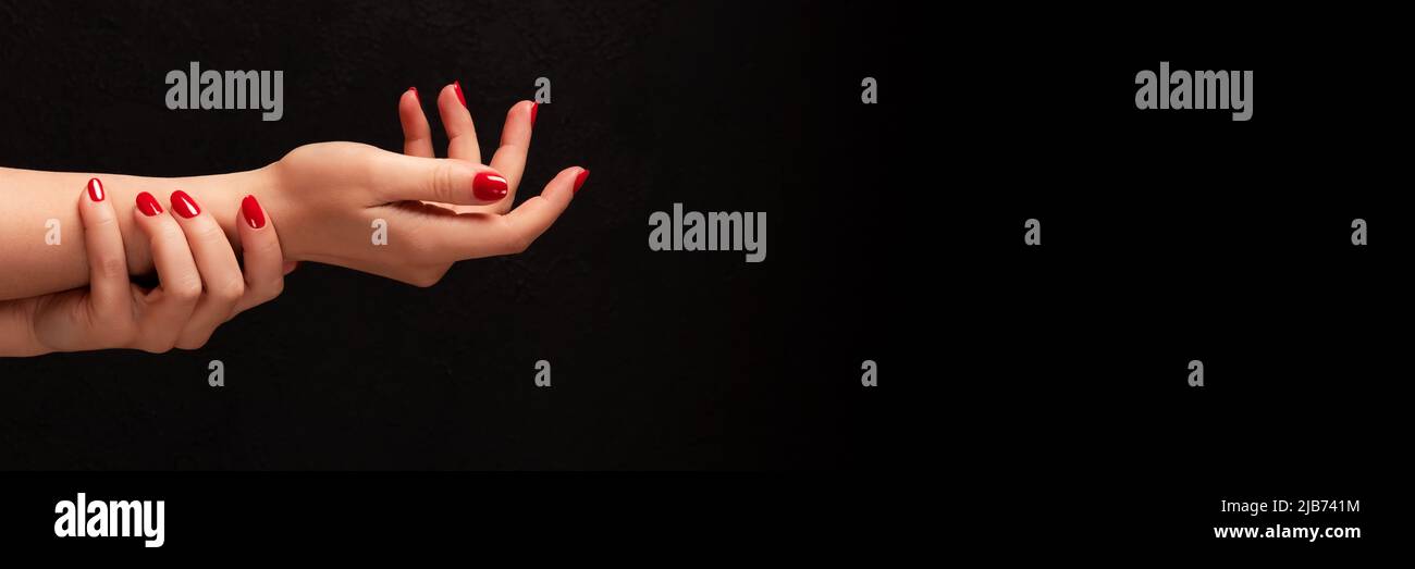 Mani femminili con manicure bello - chiodi rossi su sfondo nero scuro con banner spazio copia. Testata panoramica larga Foto Stock