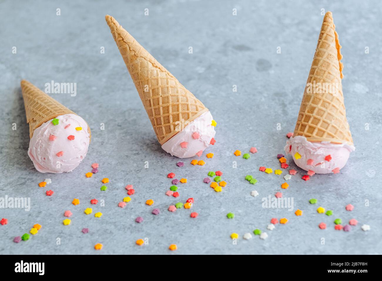 Palla di gelato rosa nel corno cospargere di stelle colorate su uno sfondo grigio. Menu estivo e dolce, piatto Foto Stock