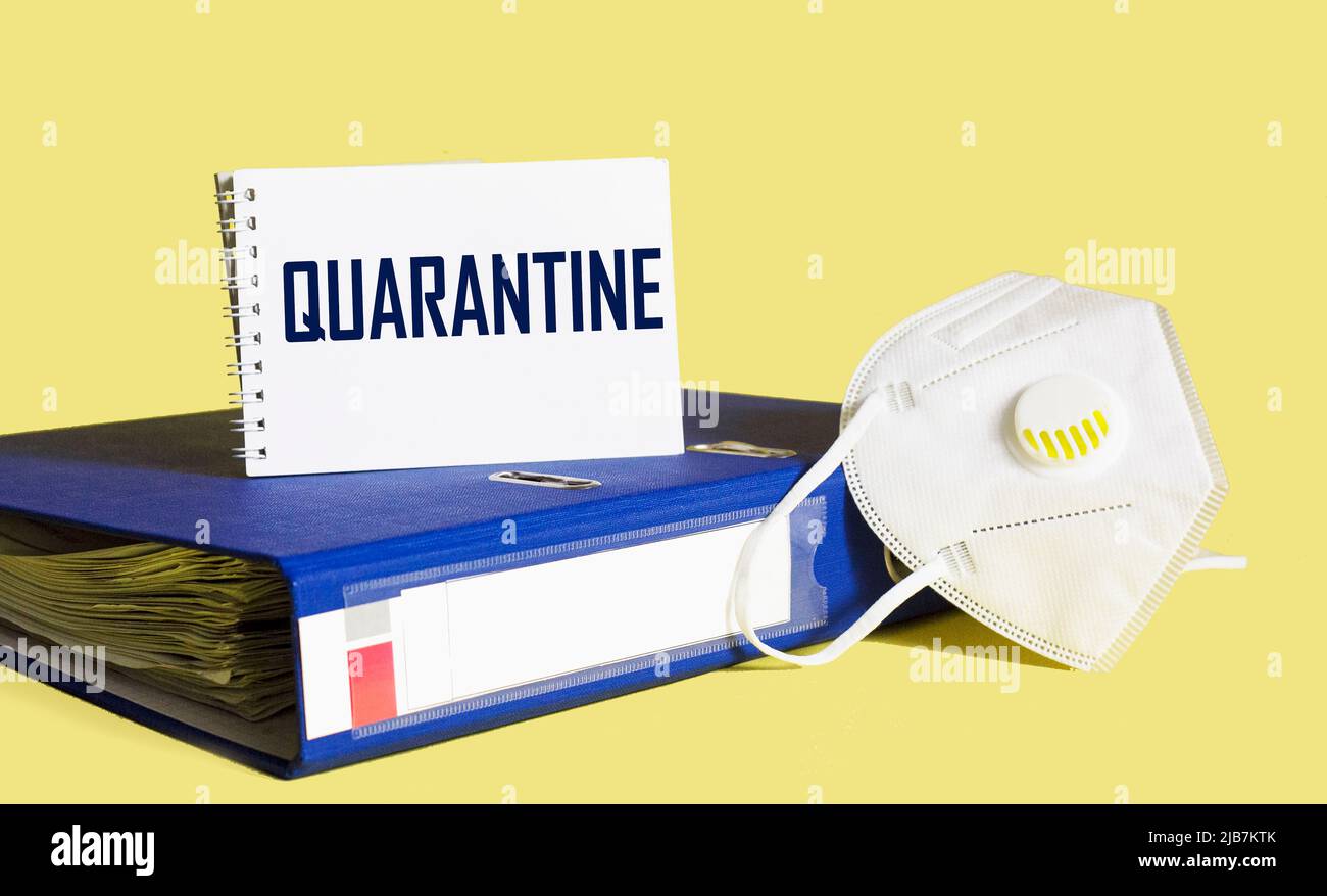 Concetto di quarantena del coronavirus. Sul desktop è presente una cartella con documenti, una maschera medica e un blocco note con LA QUARANTENA del testo Foto Stock
