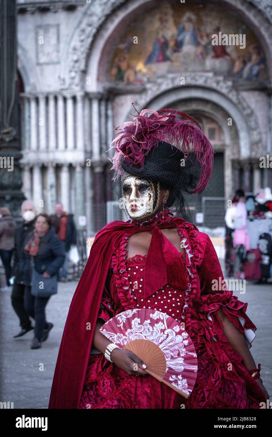 Venezia, Italia - 18.02.2022: Donna mascherata in abito rosso con piume  viola su cappello nero e ventilatore a mano al carnevale veneziano Foto  stock - Alamy