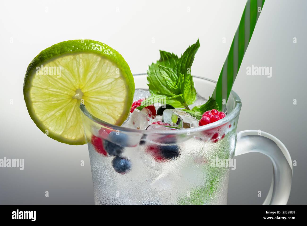 Rinfrescante cocktail estivo con ghiaccio, lime e frutti di bosco in un bicchiere di paglia Foto Stock