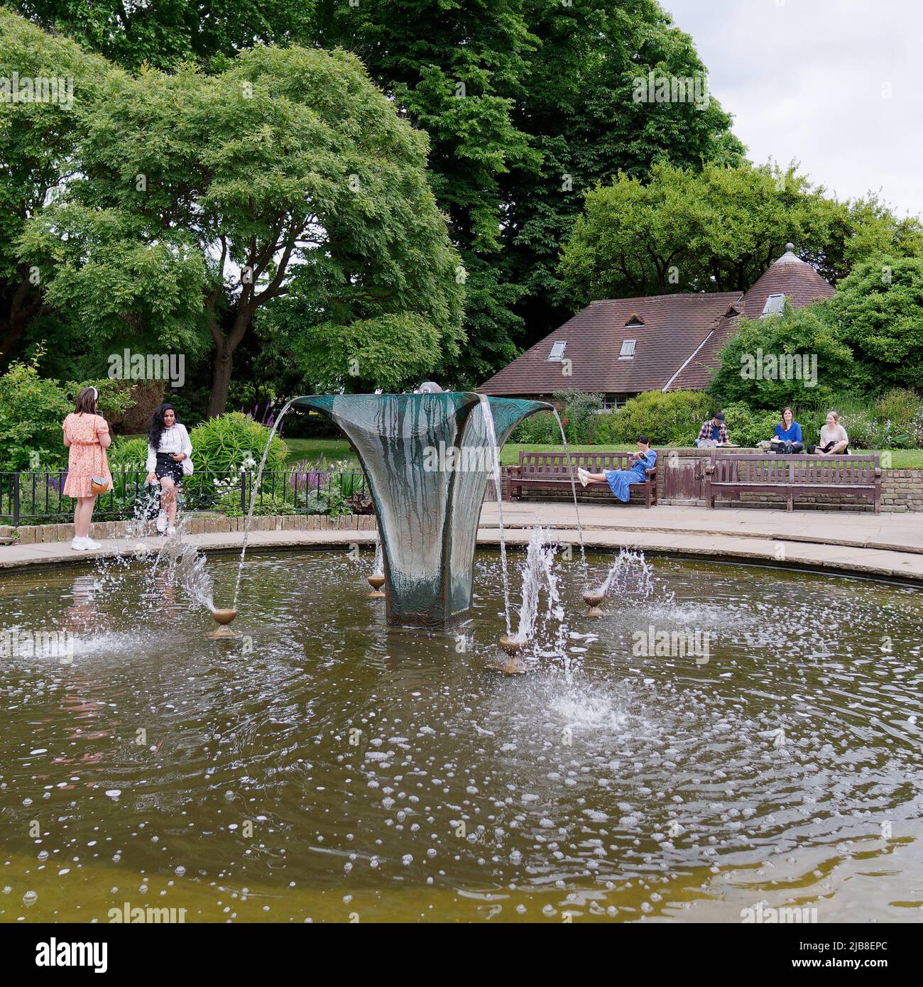 Londra, Grande Londra, Inghilterra, maggio 28 2022: Le persone che godono di una giornata di primavera soleggiata accanto alla fontana e cottage a Holland Park nel Kensington sono Foto Stock