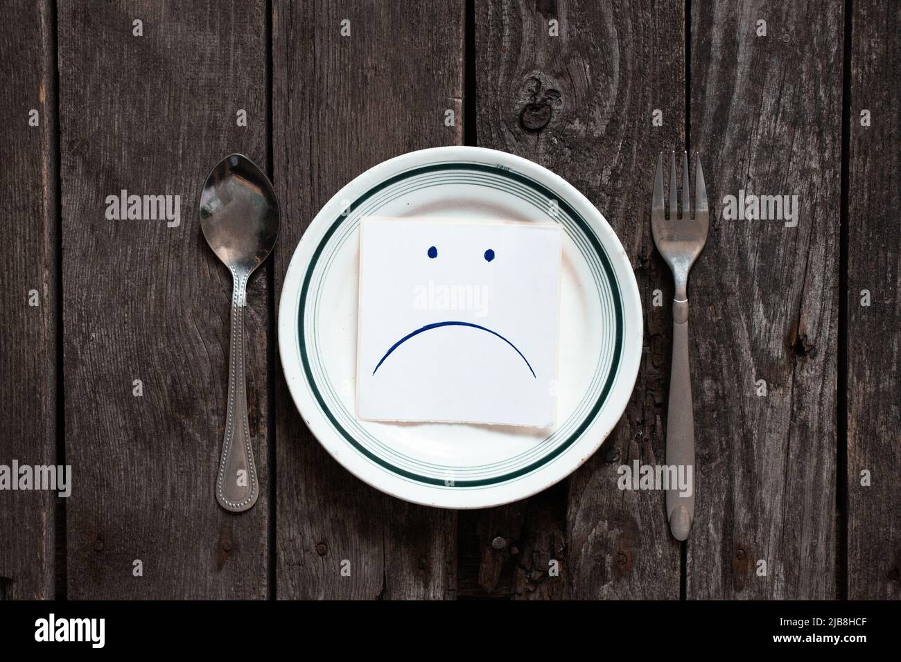 triste udibka disegnato su un pezzo di carta giace su un piatto vuoto sul tavolo, tristezza quando non c'è niente da mangiare, fame e cattivo umore Foto Stock