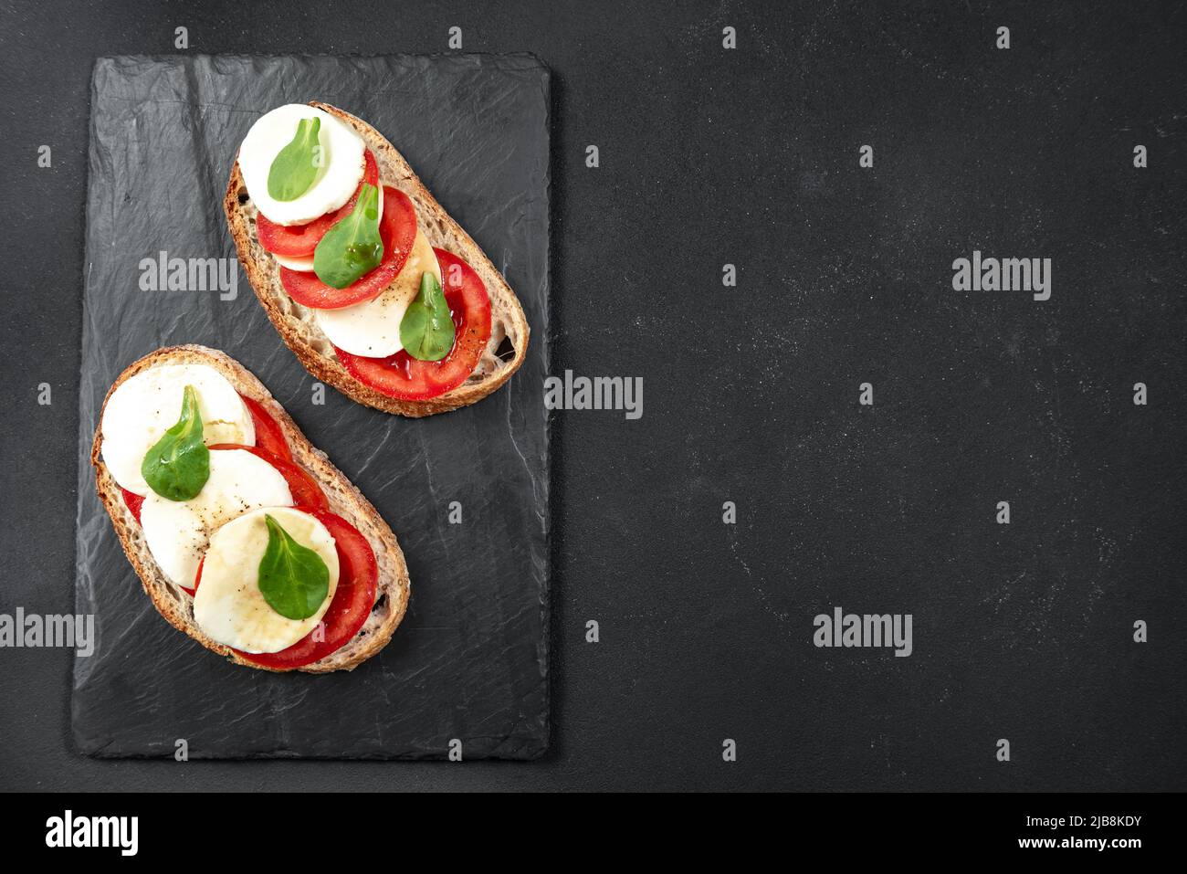 Panino italiano con macarella di basilico e pomodori su sfondo scuro su ardesia. Vista dall'alto con spazio per il testo. Foto Stock