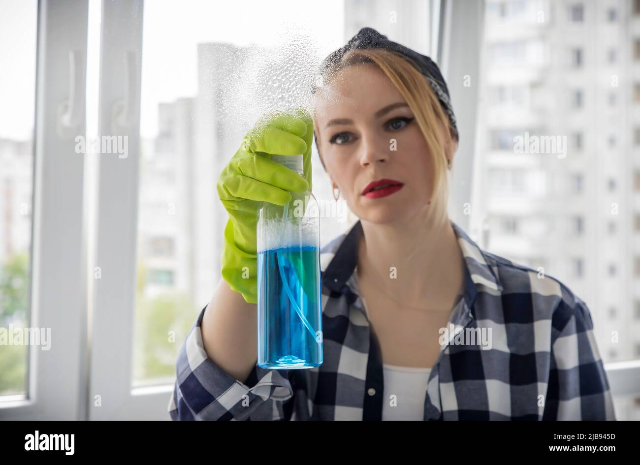 La hostess spruzza il detergente per vetri sulla finestra. Il concetto di pulizia in casa. Foto Stock