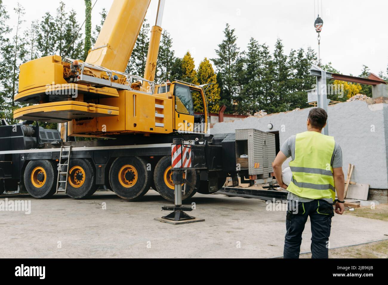 Uomo che lavora con il casco dalla parte posteriore in cantiere costruzione casa privata Ingegnere osservare il lavoro. Spazio di copia. Sollevamento con gru mobile di grandi dimensioni Foto Stock