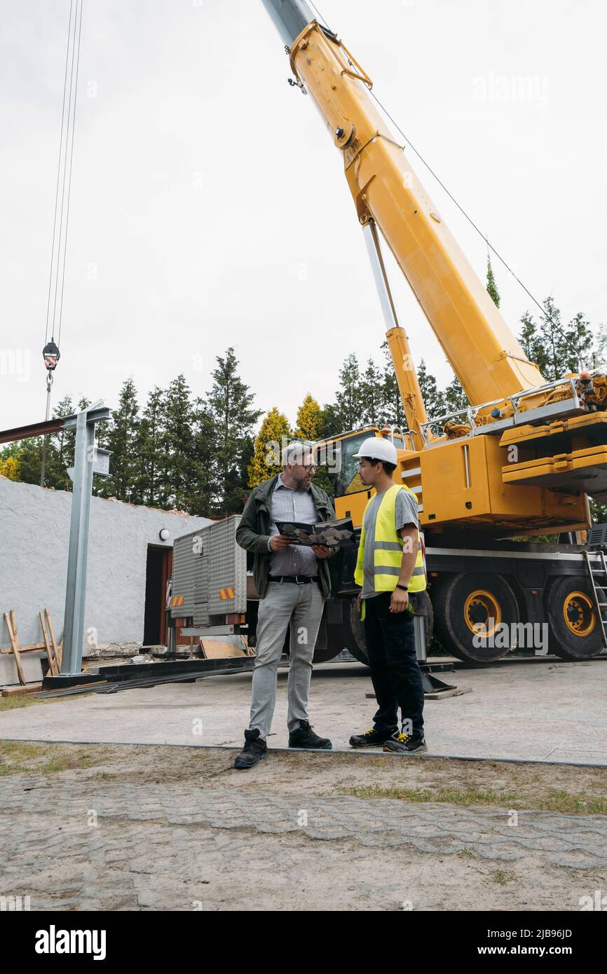 Il caposquadra e il cliente o il cliente concordano sui futuri lavori di costruzione in cantiere. Uomo che guarda nella carta, architetto che discute il progetto con il costruttore Foto Stock