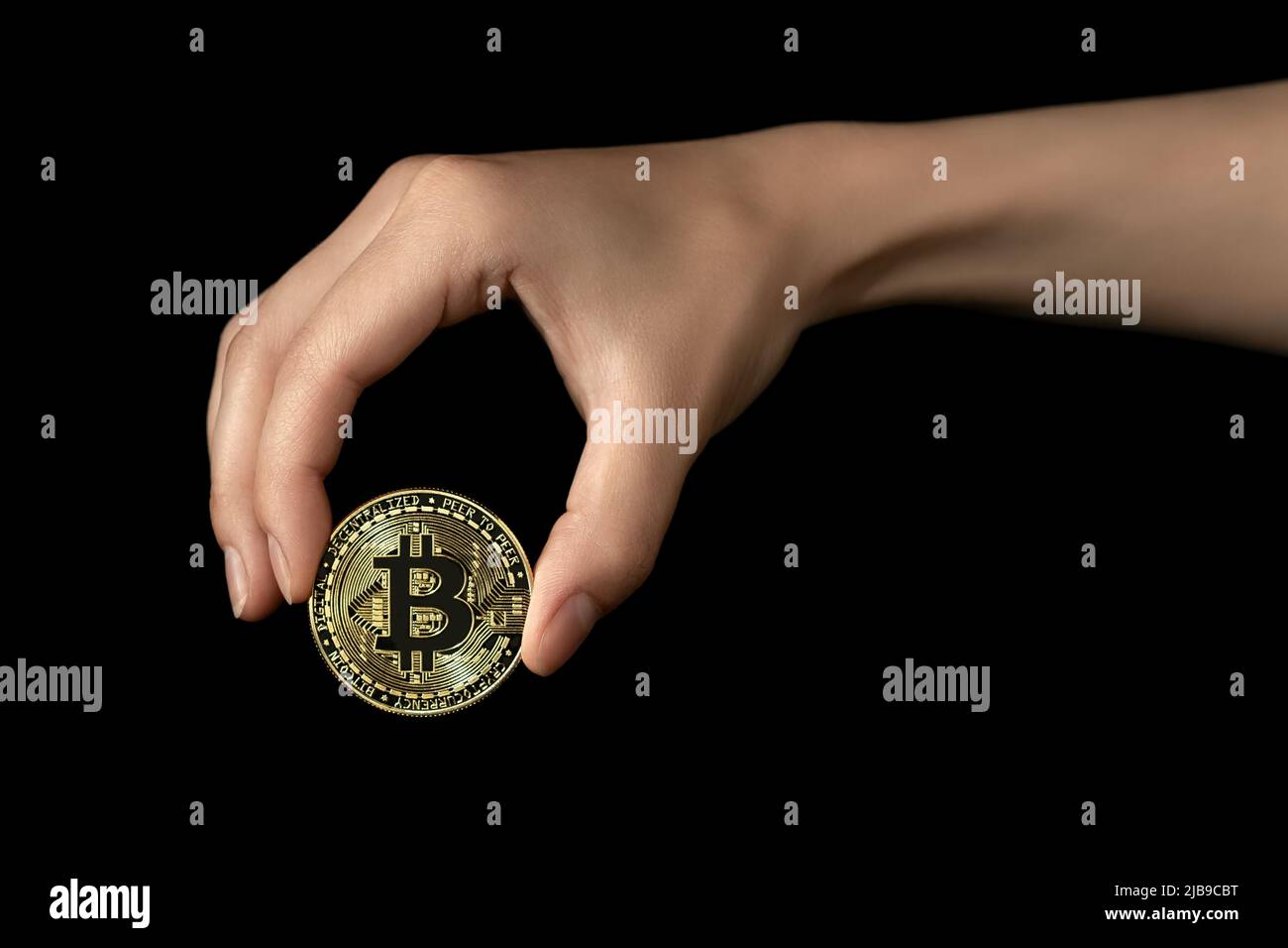 La mano della donna tiene un bitcoin nelle sue dita. Isolato su sfondo nero. Foto Stock