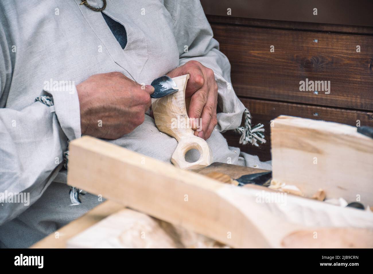 Artigiano lituano in costumi tradizionali intagliando una tazza di legno e vendendo i suoi manufatti e oggetti in legno fatti a mano in un mercato locale di strada Foto Stock