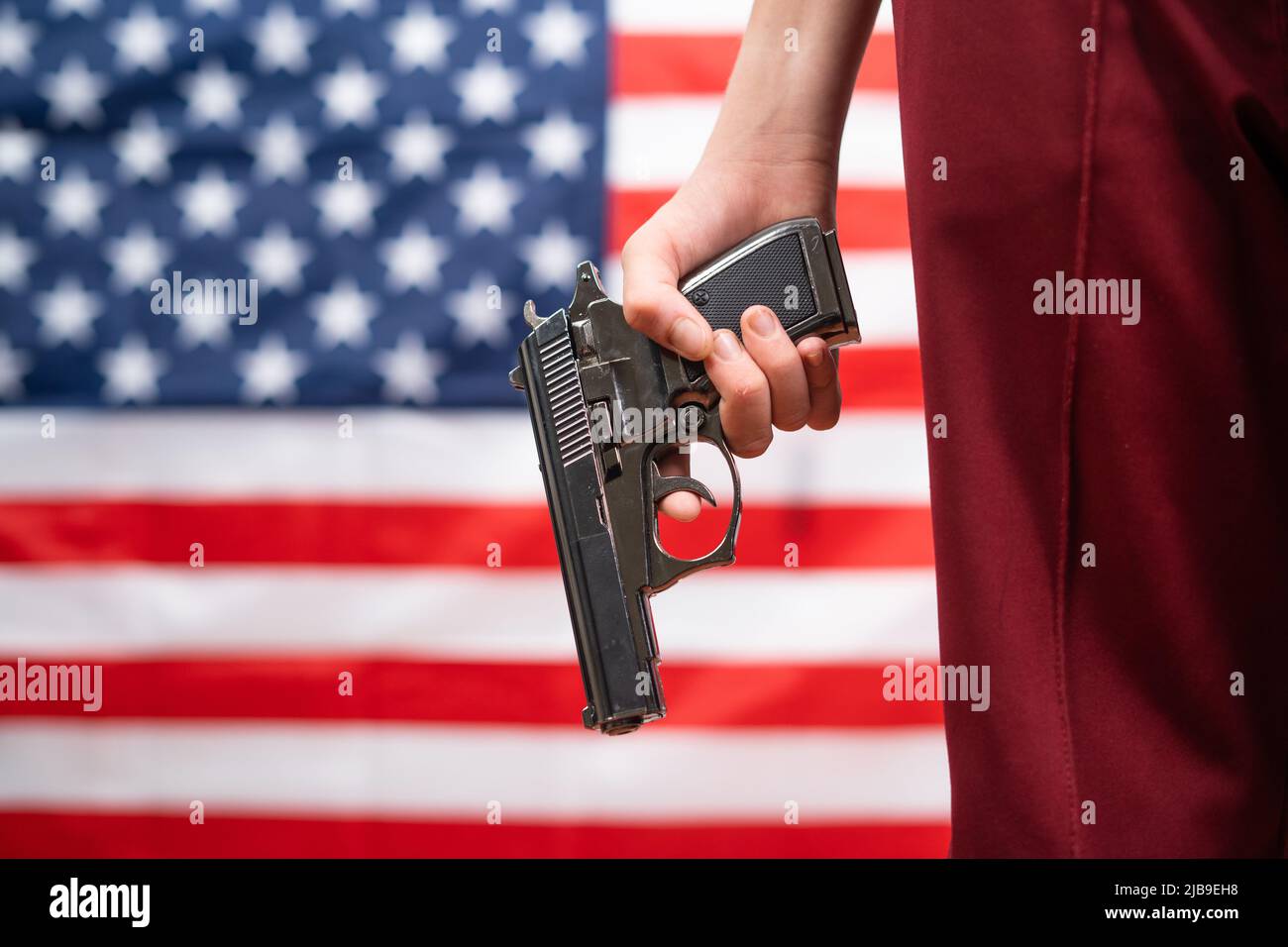 Teenager bambino che tiene la pistola contro US o la bandiera americana come sfondo - concetto di violenza delle armi Foto Stock