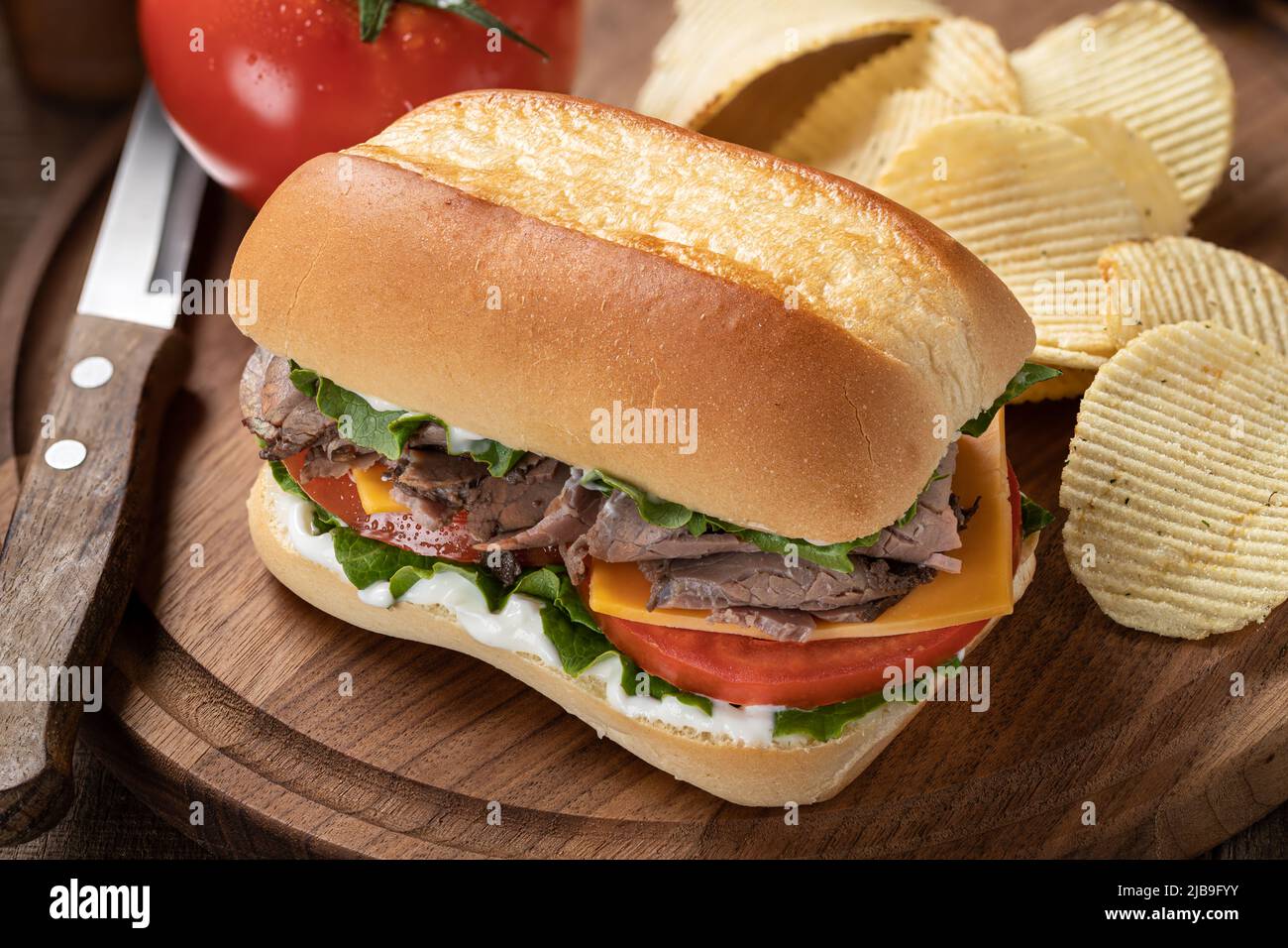 Sandwich di manzo arrosto con formaggio, pomodoro e lattuga su un tagliere di legno Foto Stock