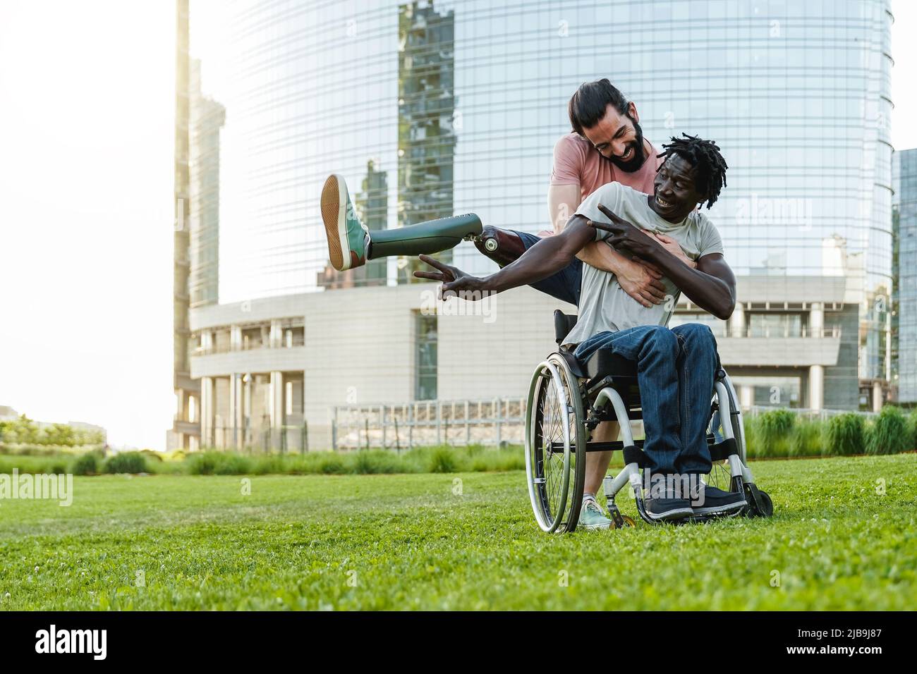 Felice amici diversi con disabilità divertirsi all'aperto al parco della città - Focus su uomo africano su sedia a rotelle Foto Stock