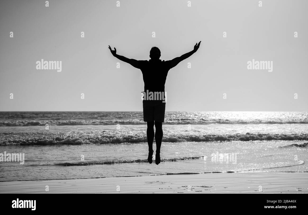 silhouette di uomo atletico che salta con mani rialzate sulla spiaggia estiva, libertà Foto Stock