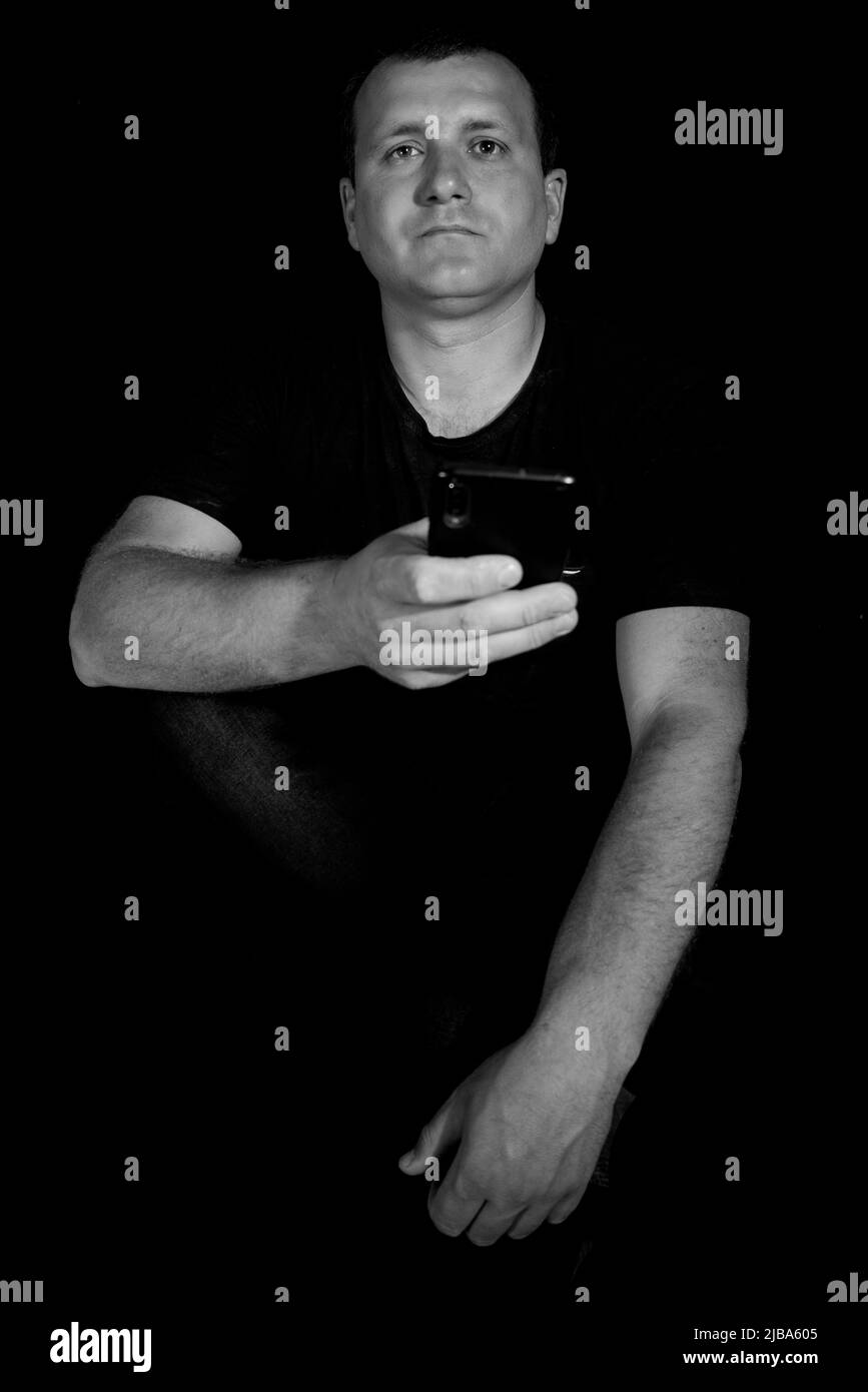 Uomo con telefono su sfondo nero. Foto Stock